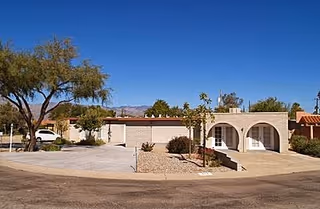 Single-story ranch-style home with arched front entry, attached garage and desert landscaping under a clear blue sky.