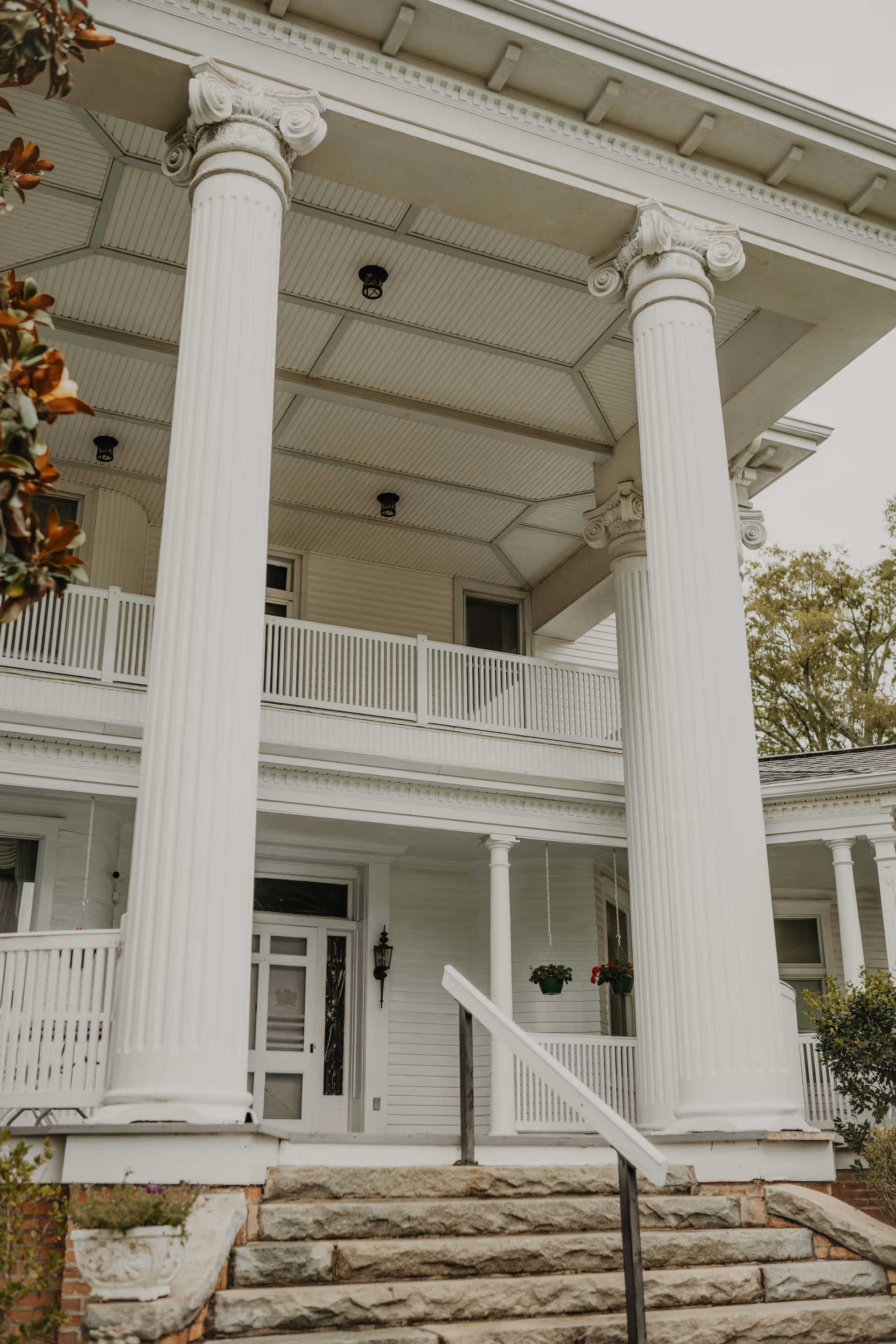 Front facade of a white colonial-style building with tall Ionic columns, a covered porch, and stone steps leading to the entrance.