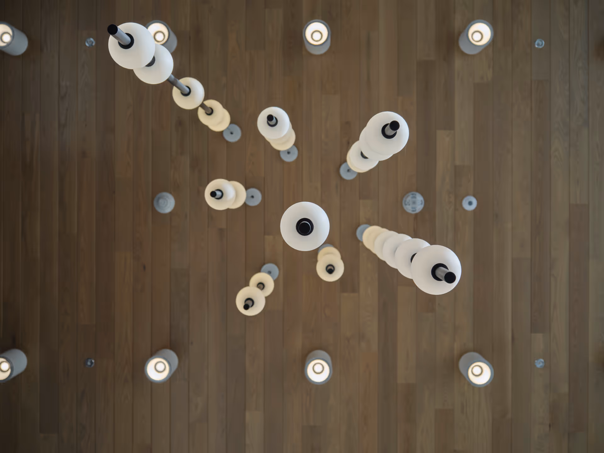 Top-down view of a modern ceiling light fixture with multiple cylindrical white lamps arranged in a pattern against a wooden ceiling background.