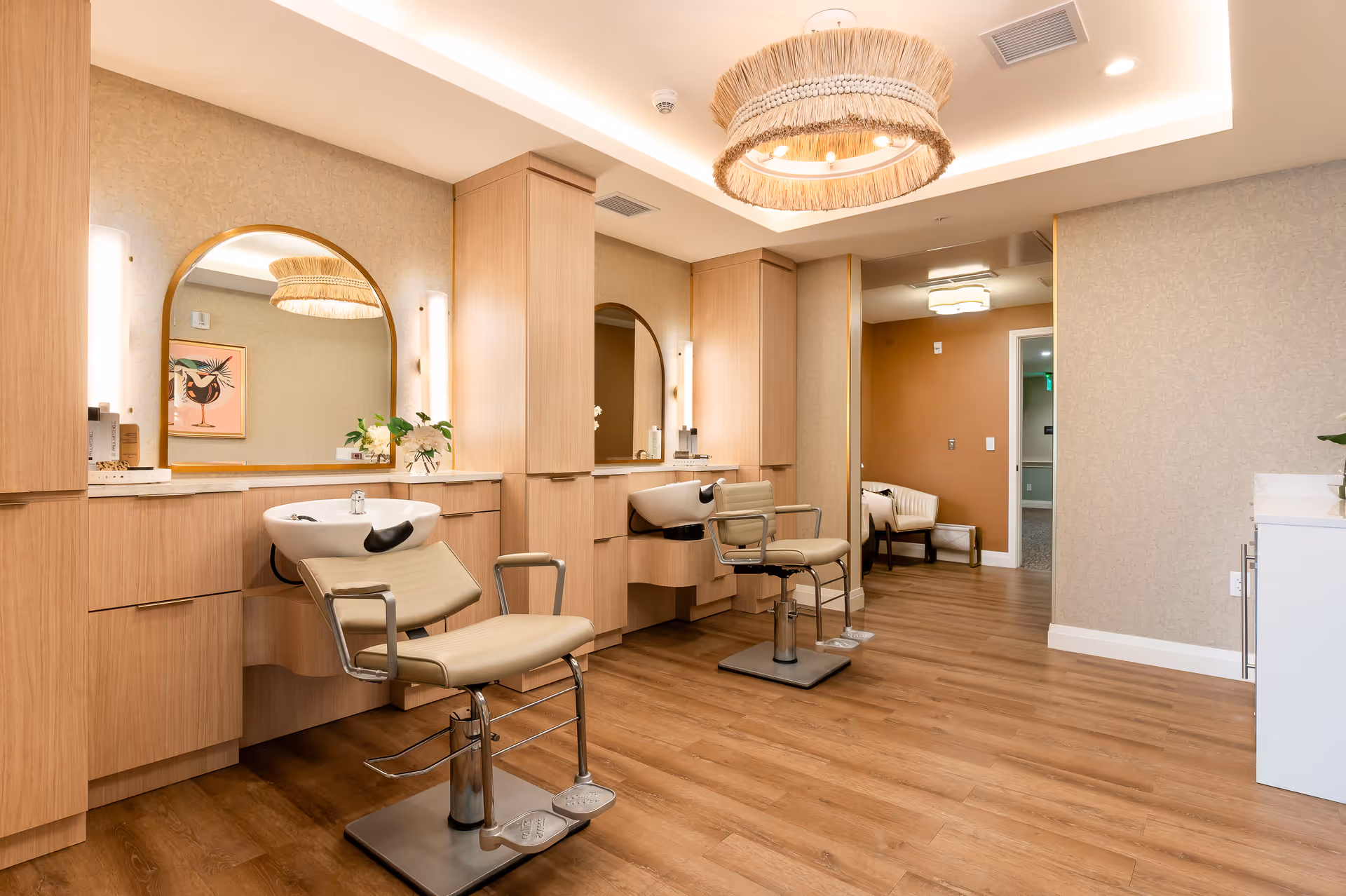 Interior salon area with two styling chairs and wash basins in front of mirrors and wood cabinetry.
