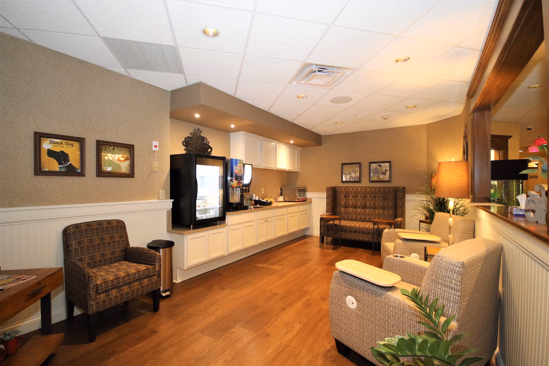 Comfortable common room with upholstered chairs, a snack/beverage station and warm lighting.