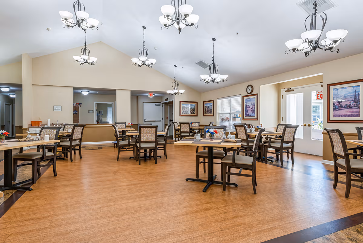 Spacious, well-lit communal dining room with multiple tables, chairs, and hanging chandeliers.