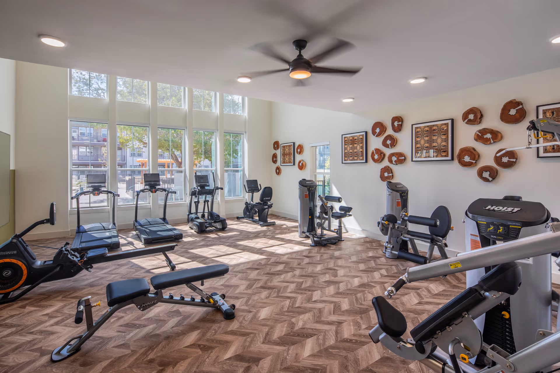 Bright fitness room with treadmills, weight machines, benches, and large windows.