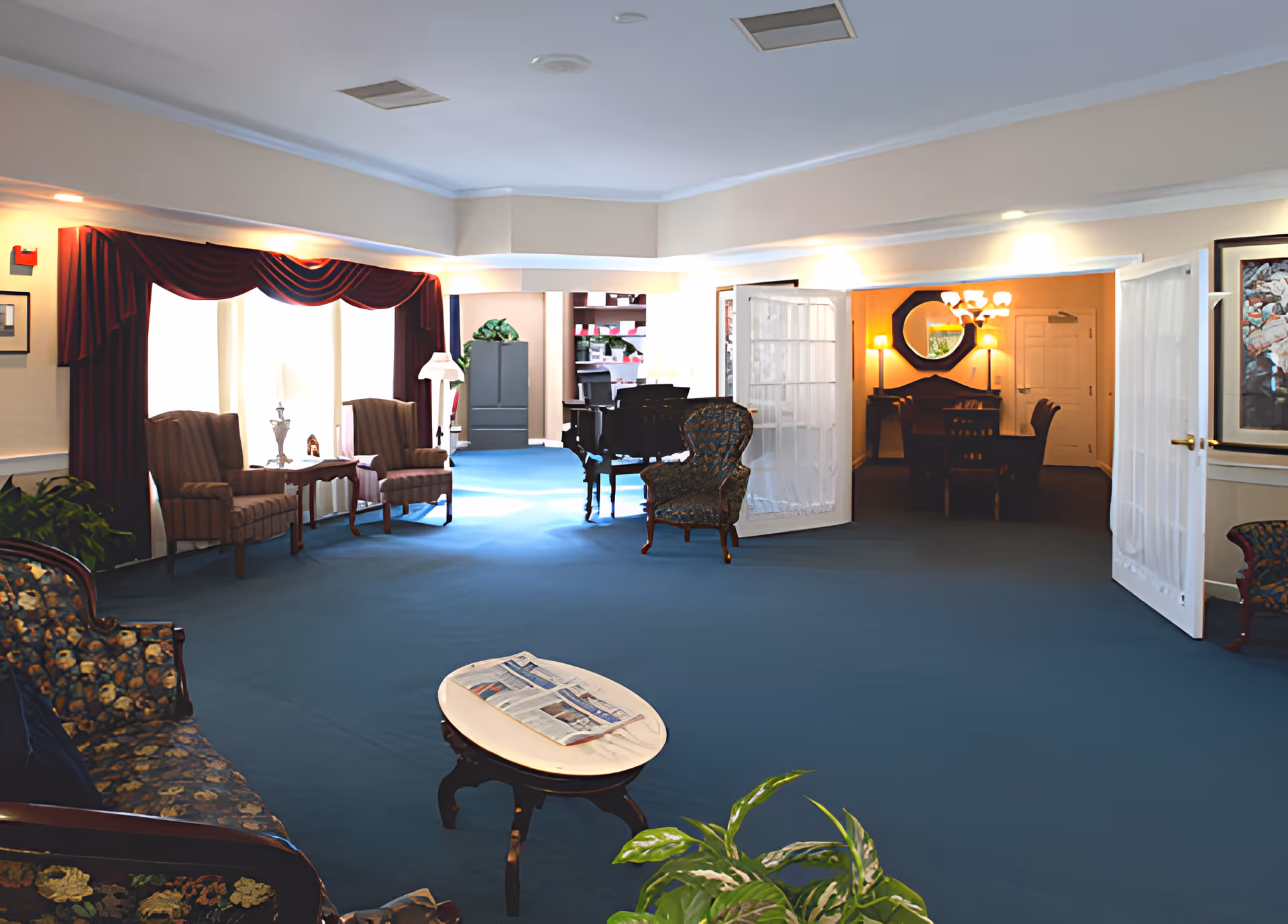 Spacious interior common lounge with upholstered seating, a coffee table, piano and an adjacent dining area.