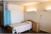 Small bedroom in a senior living facility with a bed, dresser, and privacy curtain.