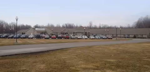 A long, low building with a parking lot and grassy foreground under a pale sky.