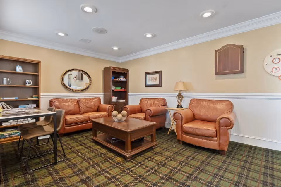 Cozy seating area with brown leather sofa and armchairs around a wooden coffee table in a carpeted lounge.