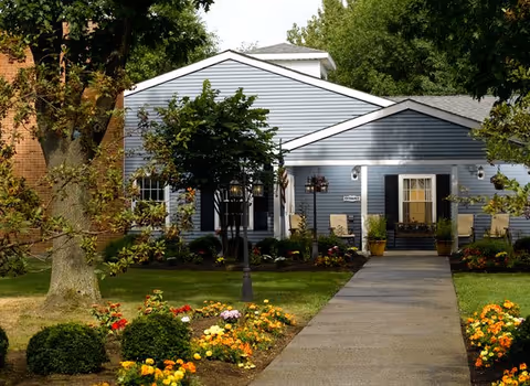 Blue, single-story senior living facility exterior with manicured lawn and colorful flower beds.