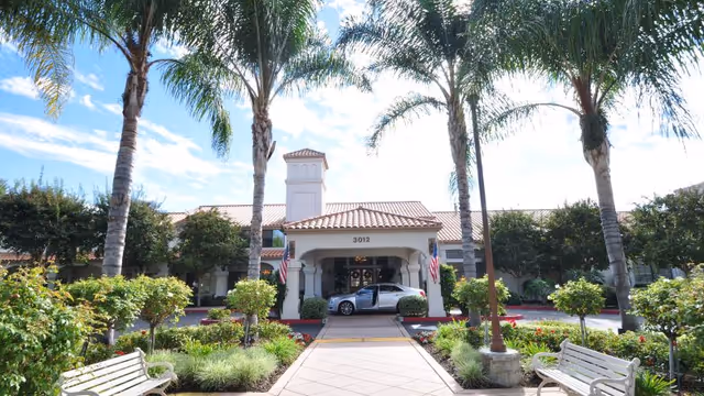 Senior living facility entrance with palm trees, benches, and a covered driveway.