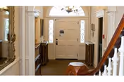 Well-lit interior foyer with a white front door flanked by sidelights, a staircase railing, and console tables.