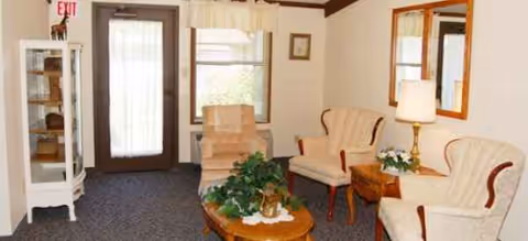 Living room in Woodlands of Findlay Assisted Living with beige chairs and plants.