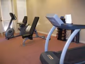 Small fitness room with a treadmill, exercise bike, weight bench, and a rack of dumbbells.