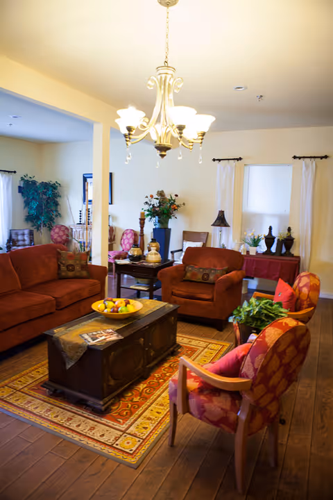 Cozy living room with red upholstered sofas and armchairs arranged around a wooden coffee table on a patterned rug beneath a chandelier.