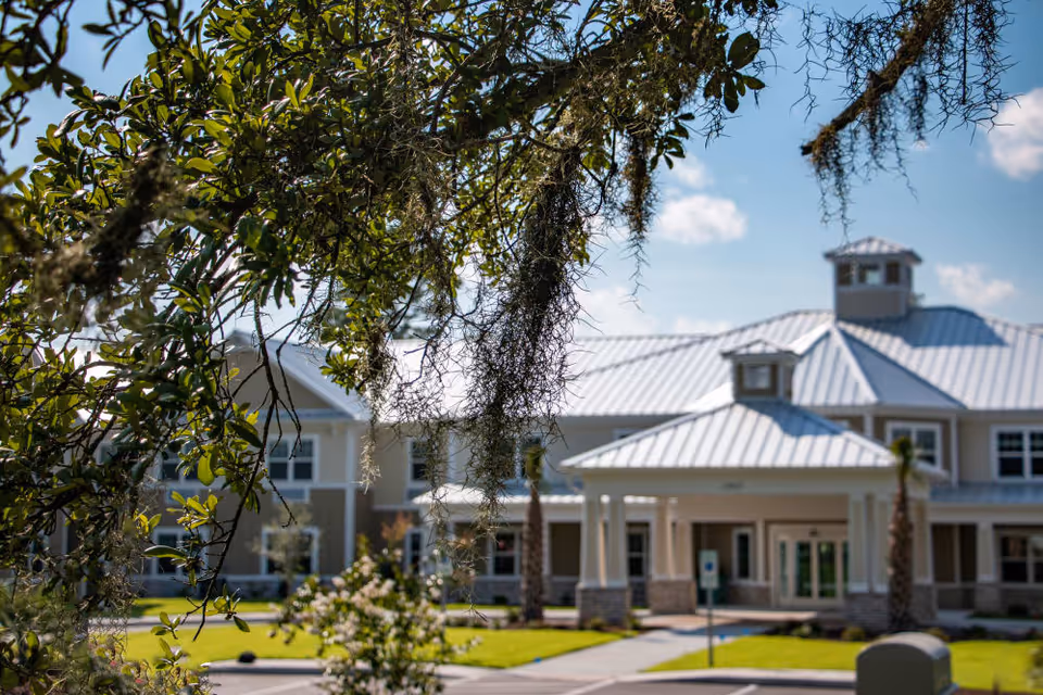 Front exterior of a senior living facility building framed by tree branches and hanging Spanish moss.