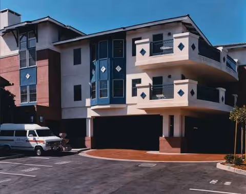 A modern multi-story senior living facility exterior with balconies and a curbside driveway.