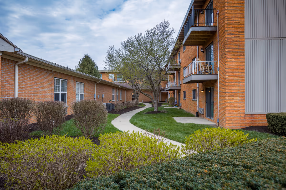 Pinnacle West Apartments exterior courtyard with brick buildings, balconies, and trimmed landscaping.