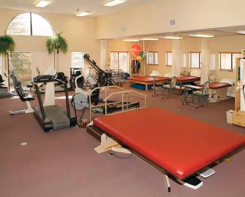 A well-equipped senior living fitness center with treadmills, exercise mats, and therapy equipment.