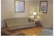 Sitting area with a green striped sofa, matching armchair, side table with a lamp, and two framed floral prints on the wall.