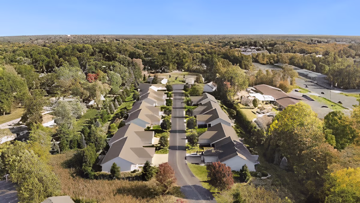 Aerial view of a row of single-story residences arranged along a central driveway surrounded by trees and greenery.