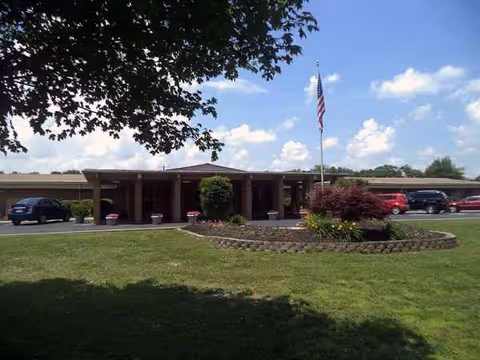 Exterior view of Sweetwater Nursing Center entrance with lawn, flagpole, and parked cars.