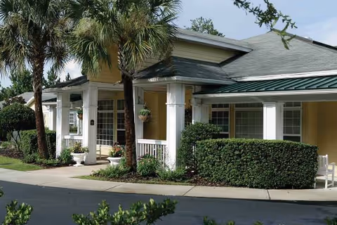 Front view of a senior living facility with columns, hedges, and palm trees.