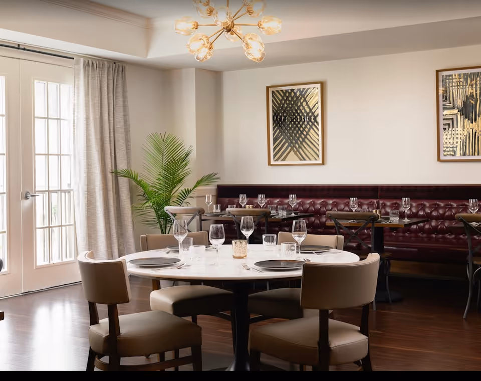 Elegant dining room with a round set table, leather chairs, a tufted banquette, and framed artwork on the walls.