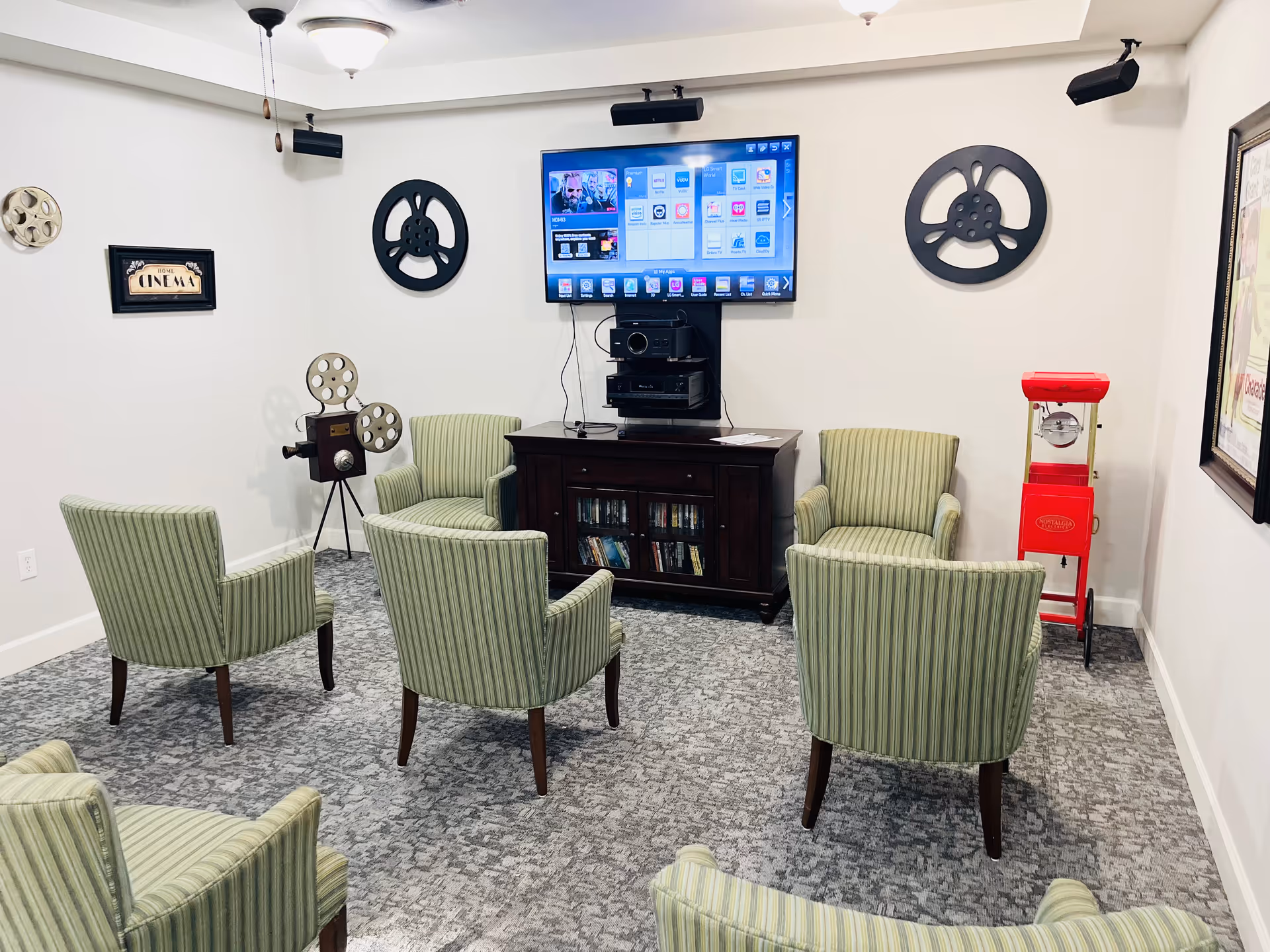 Media room with green striped chairs arranged facing a wall-mounted TV, vintage film reels on the walls and a red popcorn machine.