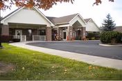 Front entrance of a single-story senior living facility with a covered porte-cochere, circular driveway, and landscaped lawn.