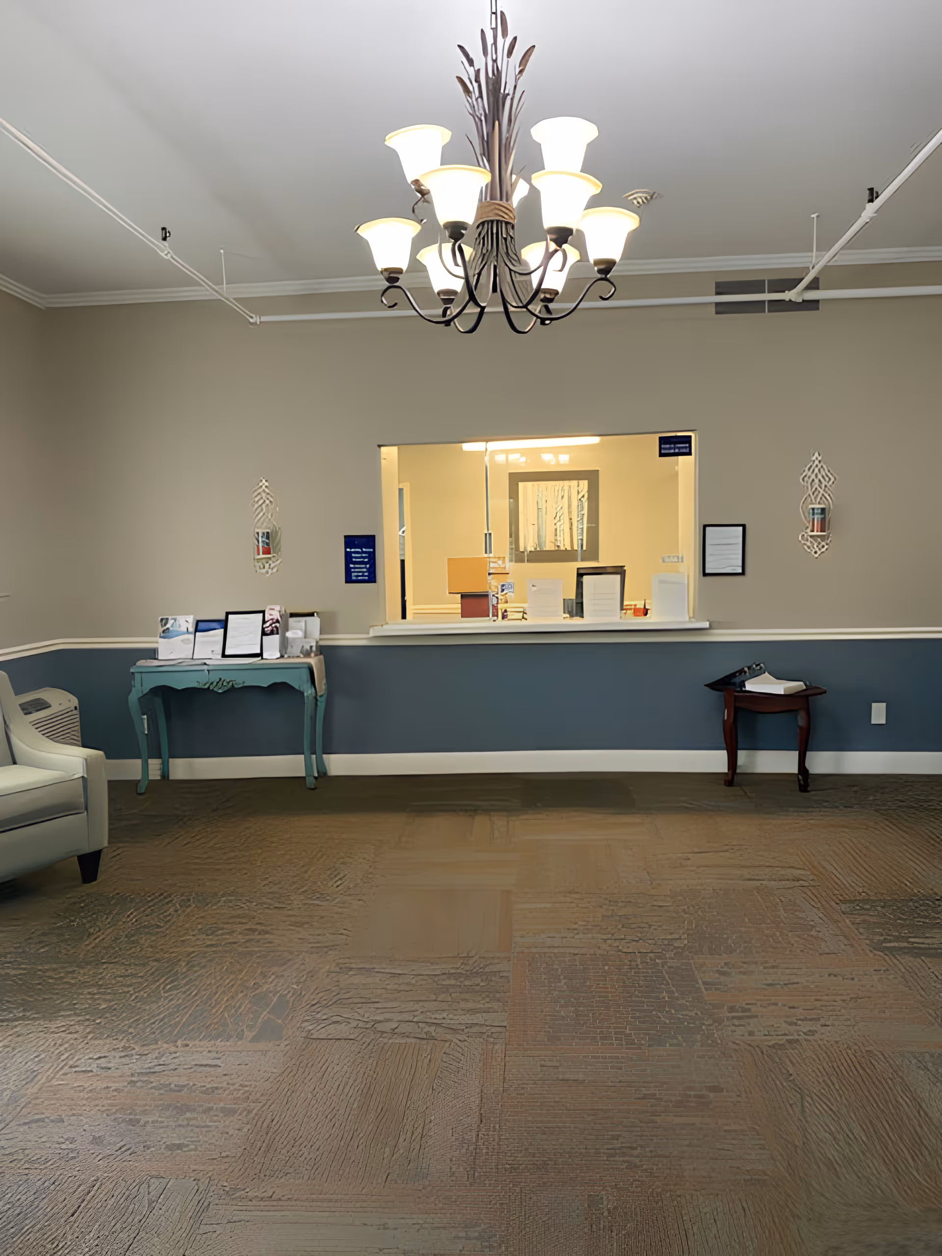 A reception lobby with a chandelier, a check-in window, seating, and small side tables.