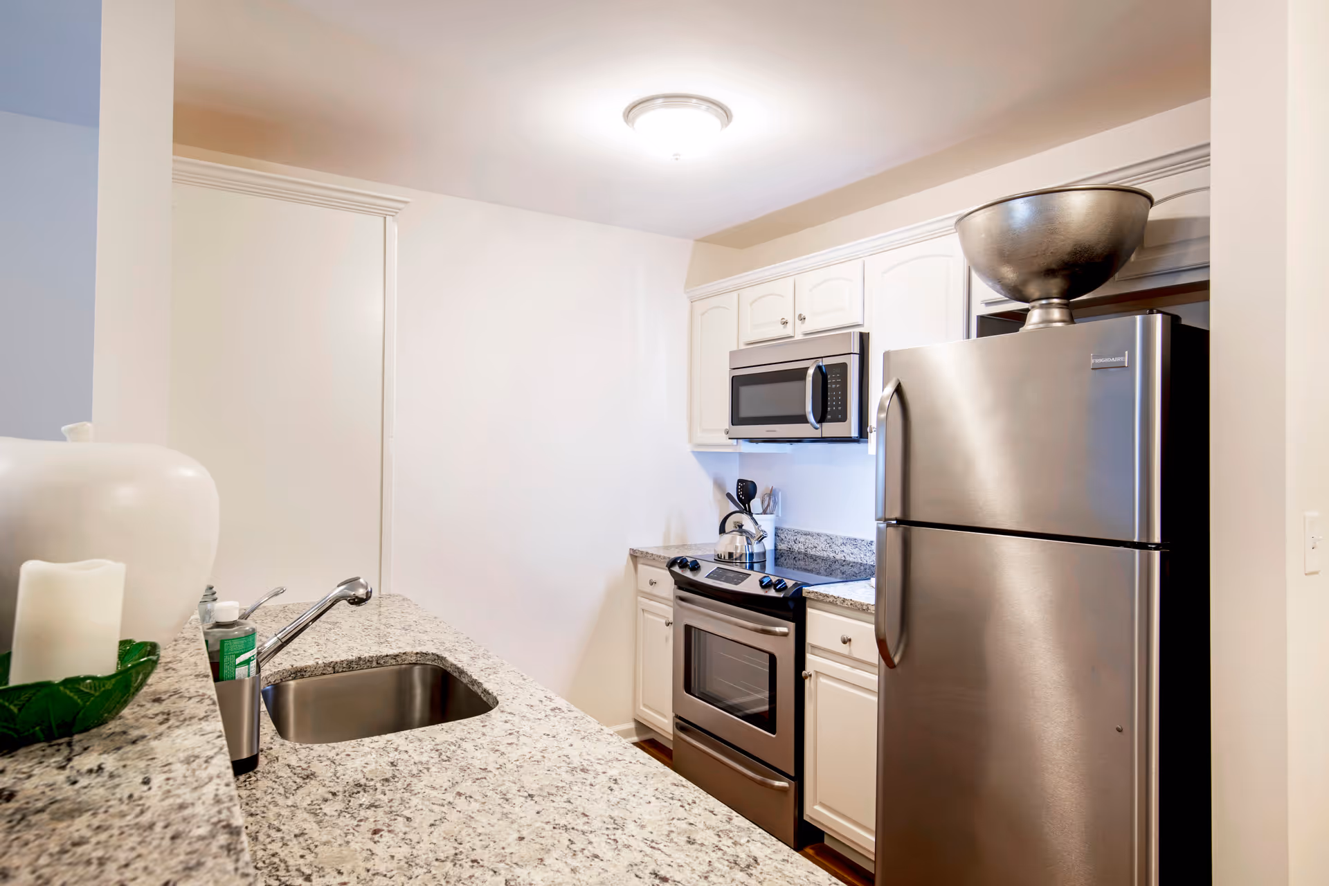 Small modern kitchen with granite countertops, stainless steel refrigerator, stove and microwave, and a sink in the foreground.