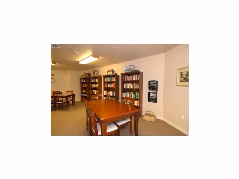 A cozy common room with wooden tables and chairs and bookshelves along the wall.