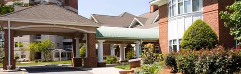 Front view of a brick senior living facility with a covered entrance and landscaping.