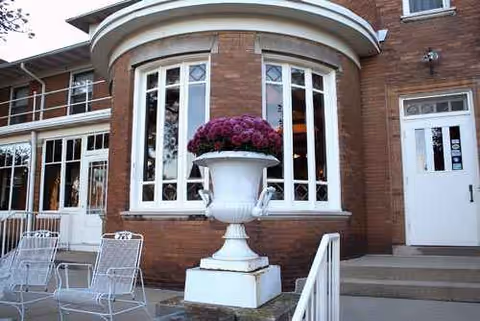 Brick senior living building entrance with arched windows and a white urn planter.