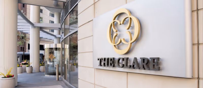 Exterior entrance of The Clare showing its logo and name on a wall beside a glass revolving door.