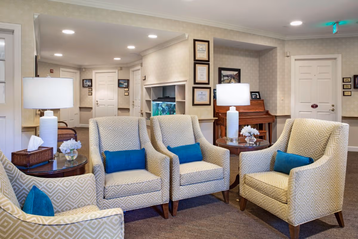 Comfortable seating area with four patterned armchairs and teal pillows arranged around side tables and lamps in a senior living common room.