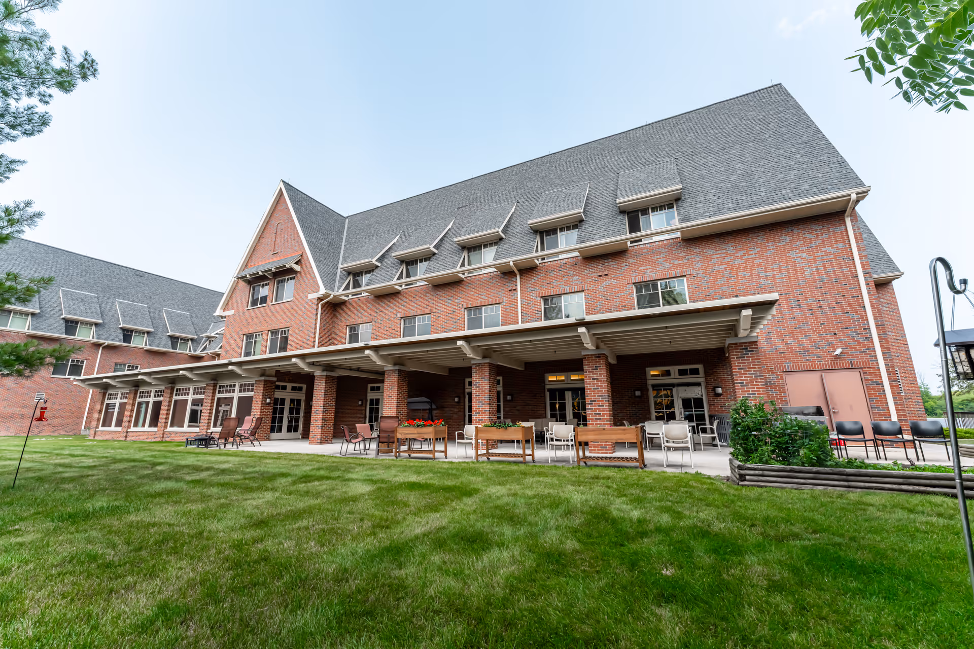 Brick senior living building with a covered patio, outdoor seating, and a grassy lawn.