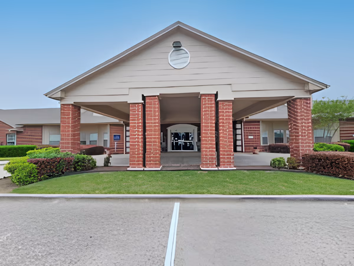 Front exterior view of Morada Burleson facility showing a covered entrance with brick pillars, manicured green lawn, and clear blue sky.