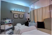 Calm treatment room with a massage table, rolled towels on a cart, a reclining chair, and a wall sign that reads 'RELAX'.