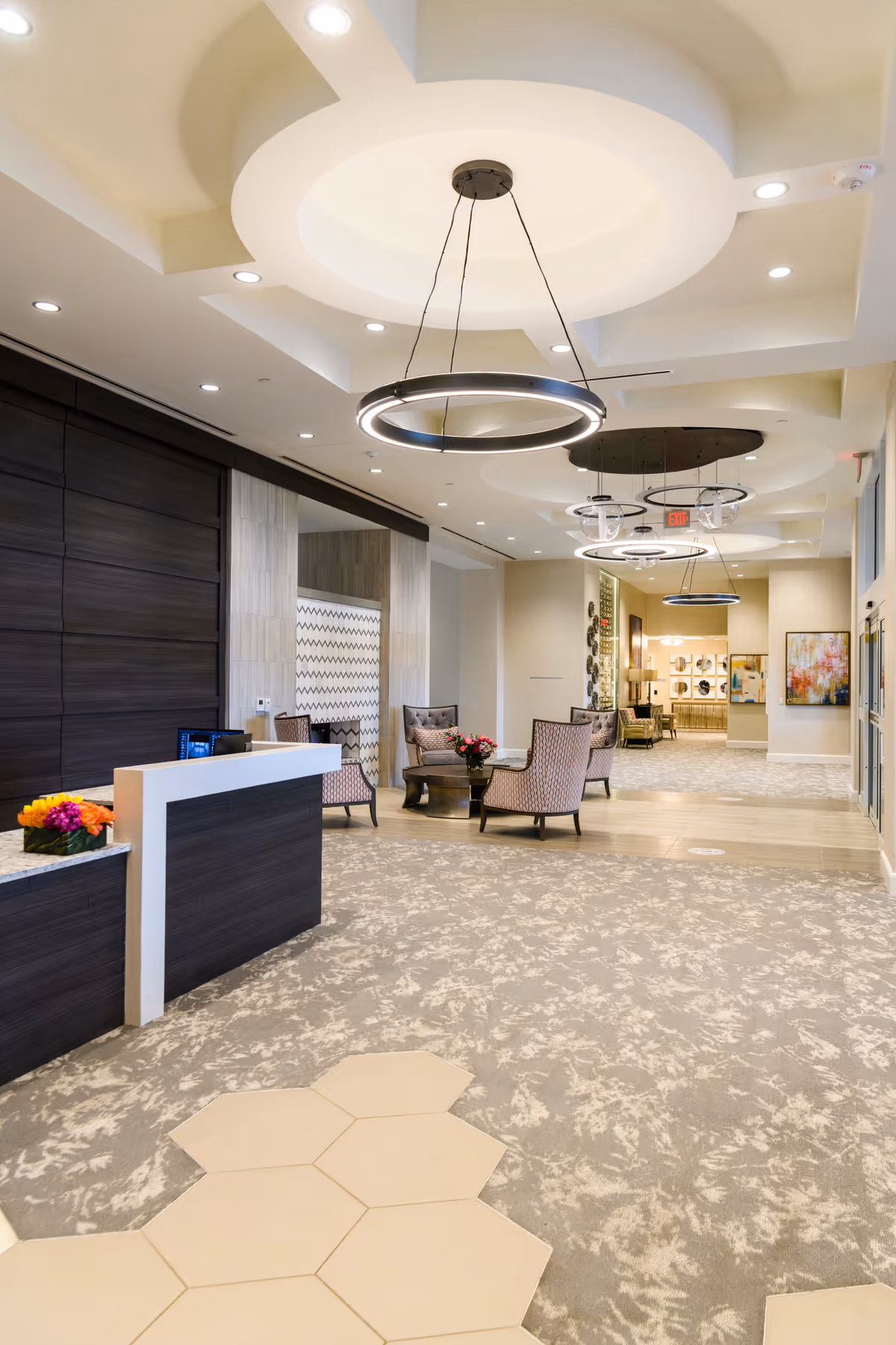Modern senior living lobby with a reception desk, seating area, and circular pendant lights under a decorative ceiling.