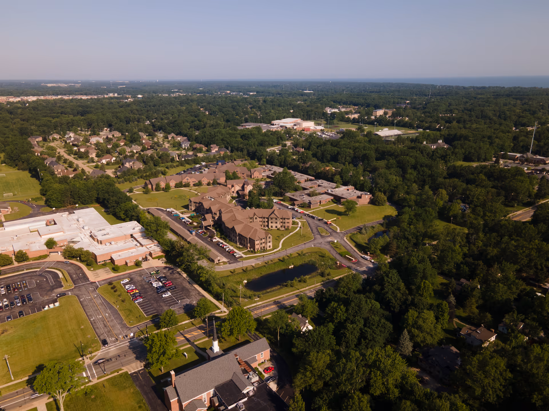 Aerial view of a suburban area with a senior living facility named Concord Reserve surrounded by trees, parking lots, roads, and nearby residential neighborhoods under a clear sky.