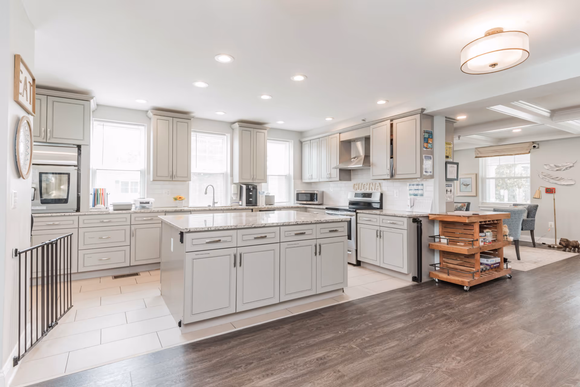 Bright modern open kitchen with a large central island, light gray cabinets, stainless appliances, and an adjacent dining area.