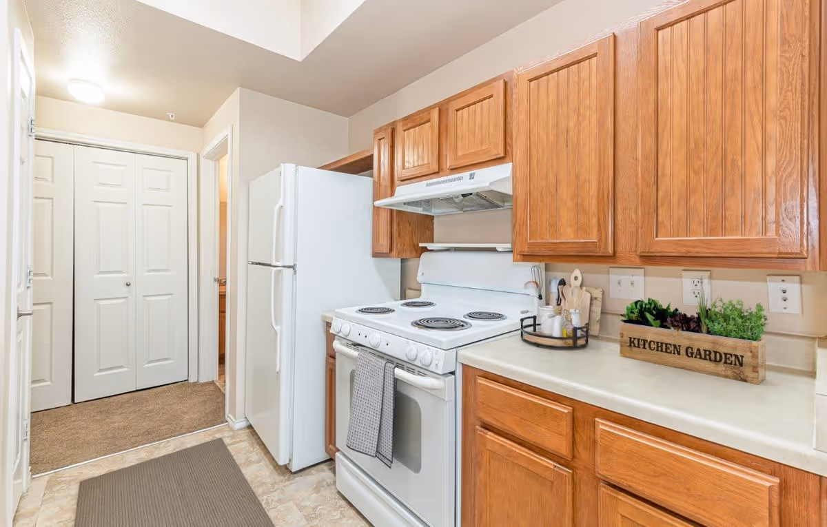 Small kitchen with a white stove and refrigerator, wooden cabinets, and a countertop planter box labeled 'KITCHEN GARDEN'.