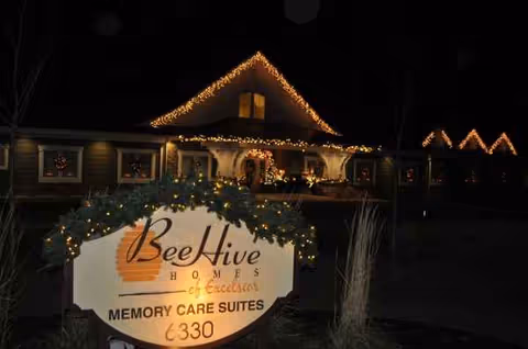 Night view of a warmly lit senior living facility with a front sign and holiday lights
