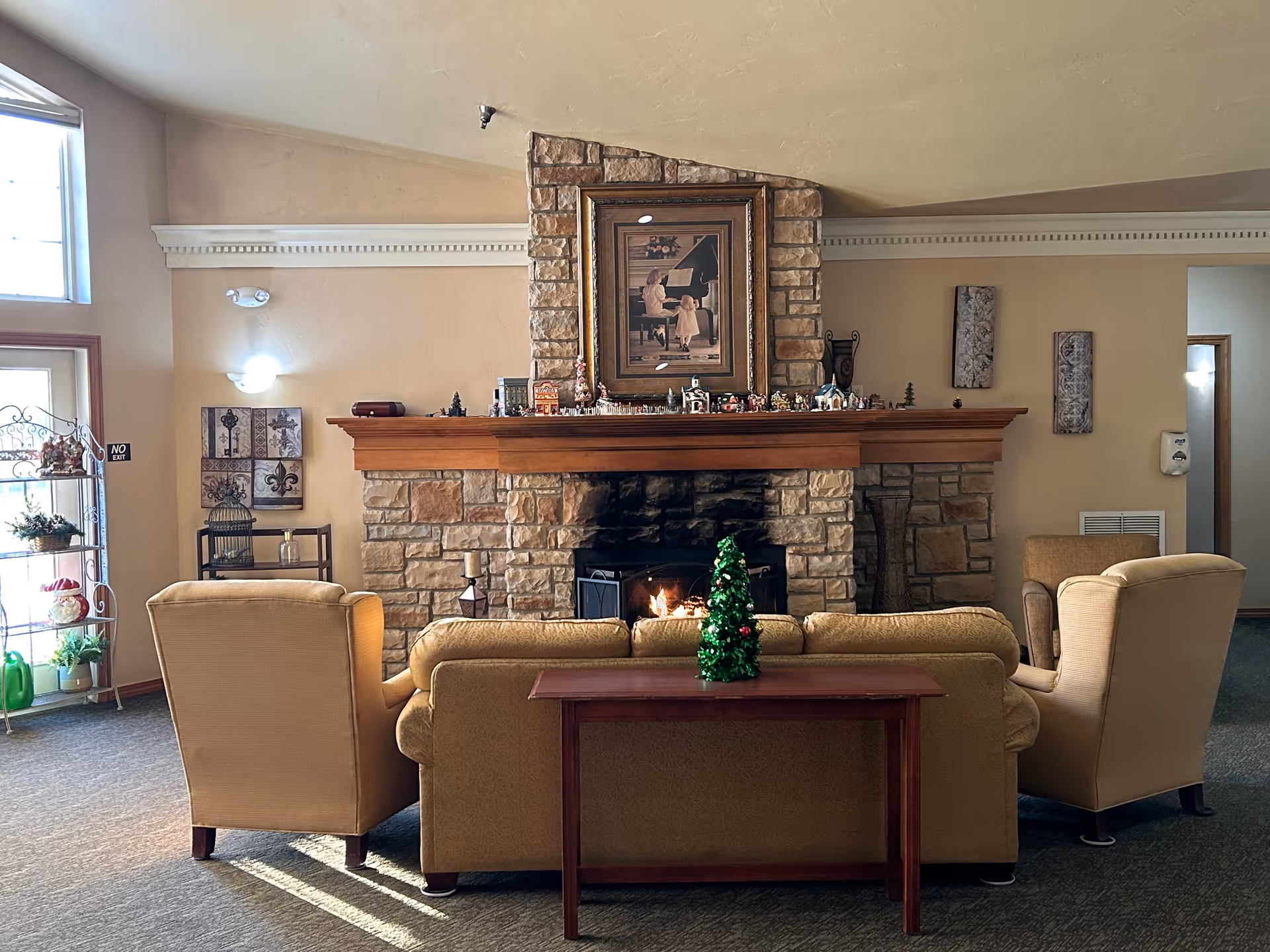 Common room with beige armchairs arranged facing a stone fireplace mantel decorated with small figurines.