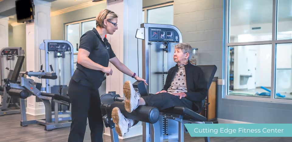 A fitness instructor helps an elderly woman use a leg-extension machine in a fitness center.