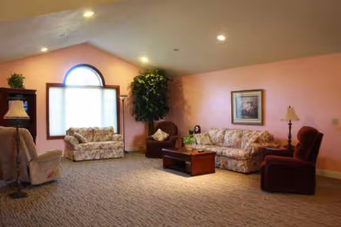 Cozy lounge with floral sofas, armchairs, coffee table, lamps, and pink walls.