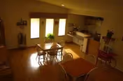 Cozy dining area with wooden table, chairs, and a small kitchen in the background.