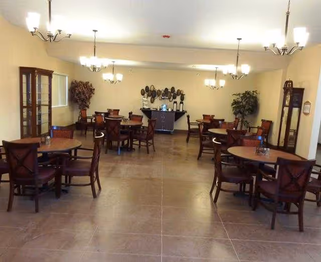 Senior living dining room with round tables, chairs, and chandeliers.