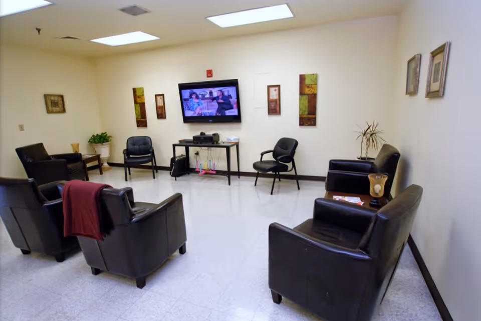 A common sitting room with leather armchairs arranged facing a wall-mounted TV, small tables, and wall decor.