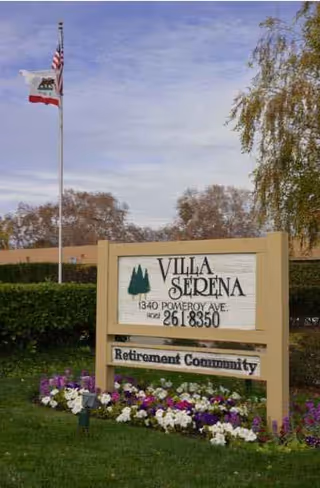 Exterior view of Villa Serena Retirement Community sign with flowers and flag.